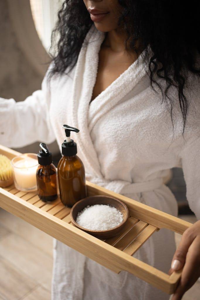 Crop black woman with skincare products, about to practice her favorite self care activities in a fuzzy white bathrobe.