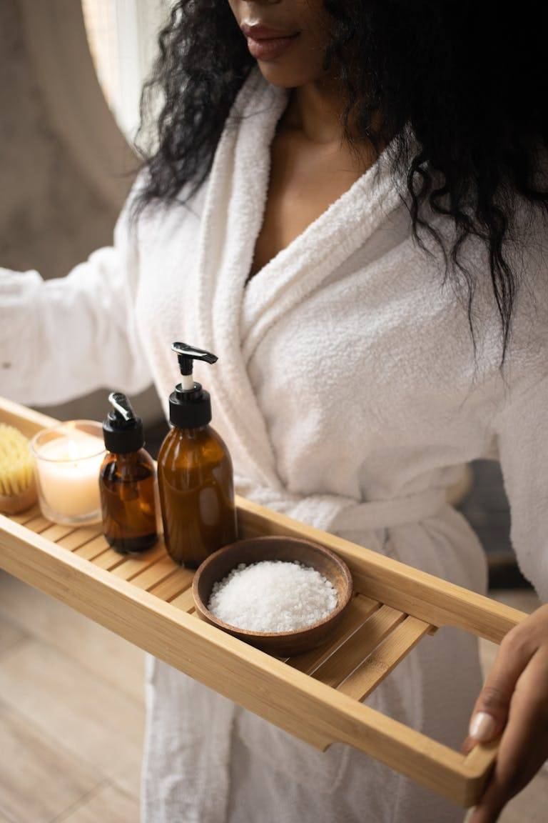 Woman carrying self care gifts on wooden tray.