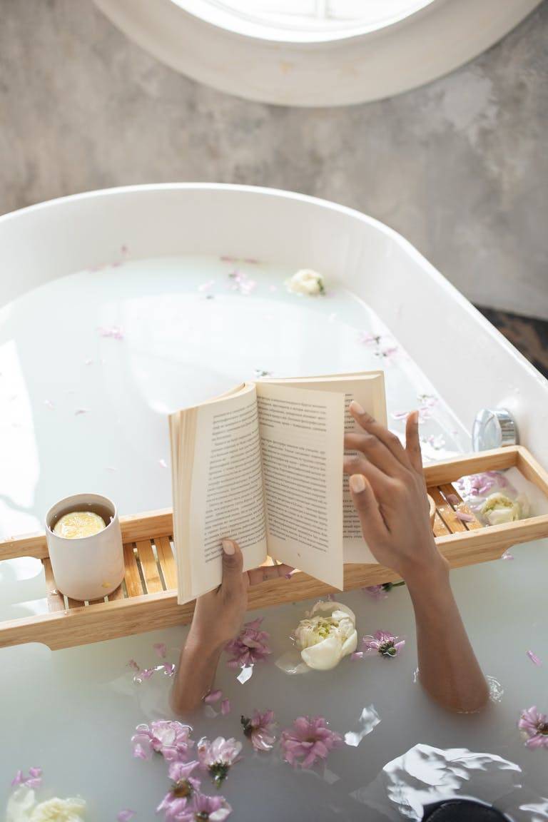 Woman with book and cup of coffee in bath, practicing self care activities that reduce stress.