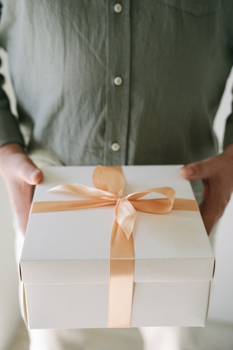 A person holding a white gift box with a peach ribbon, perfect for celebrations.